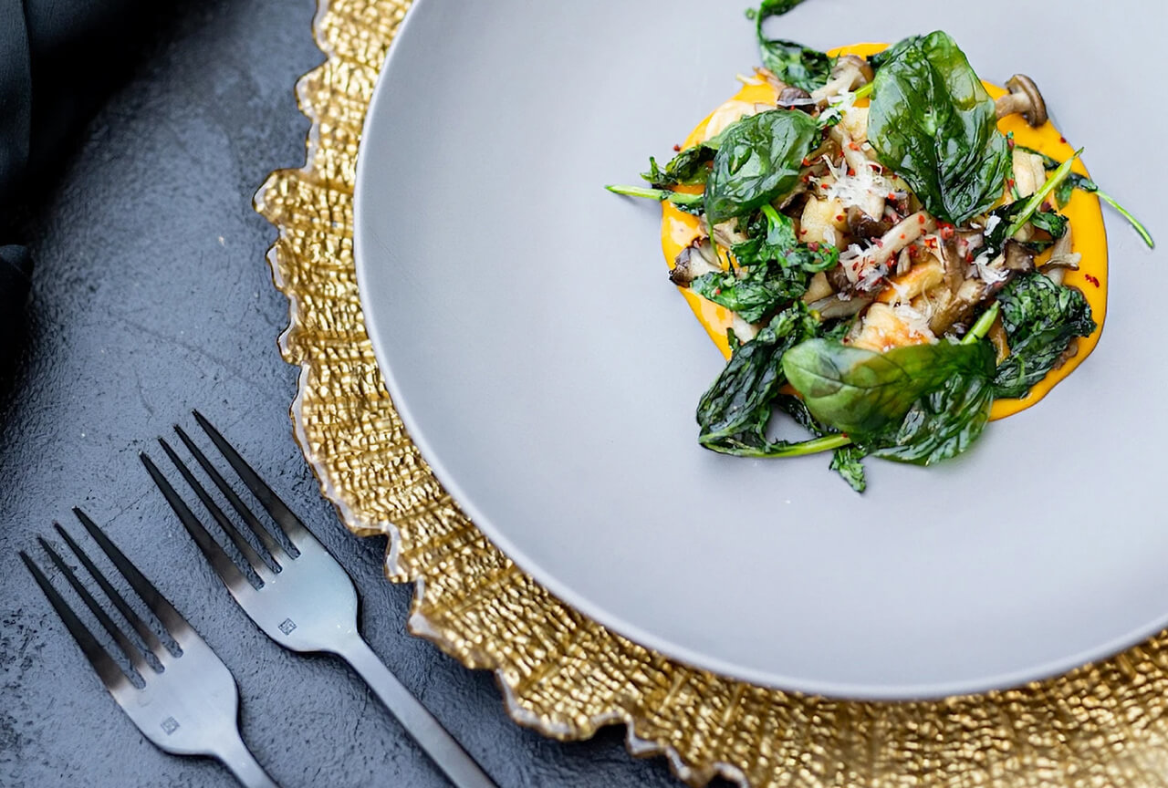Elegantly plated dish with greens and sauce on a gold charger