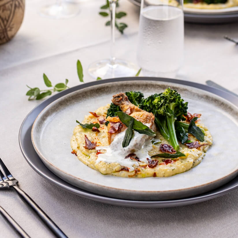 Plated dish with polenta, broccolini, and garnish on a grey ceramic plate