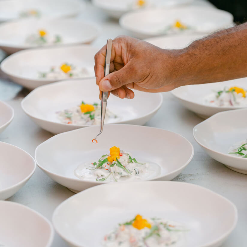Hands plating delicate appetizers into white bowls with edible flowers