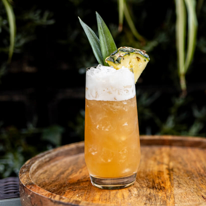 Tropical cocktail with pineapple garnish on a wooden tray