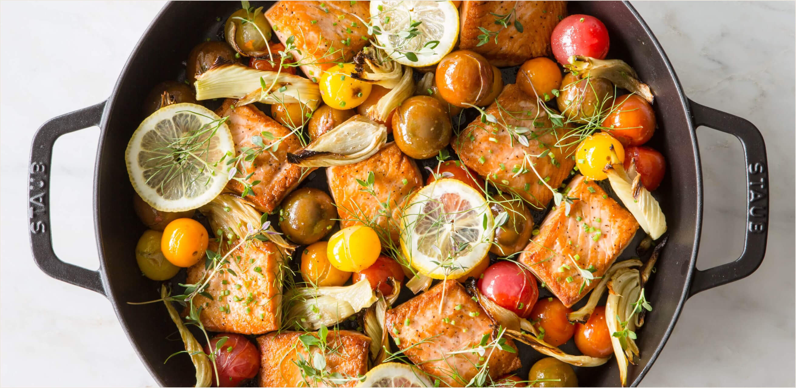 Fresh salmon with tomatoes and lemon in a cast iron pan